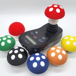 May include: A black joystick controller with six colorful mushroom-shaped buttons. The buttons are red, green, yellow, orange, black, and blue. Each button has white dots on top.
