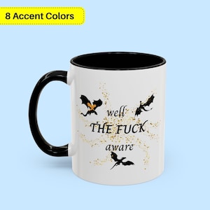 Pode incluir: Caneca de cerâmica branca com alça e interior pretos. A caneca apresenta três silhuetas de dragões pretos e o texto "well THE FUCK aware" em preto. Acentos dourados semelhantes a glitter circundam o texto e os dragões.