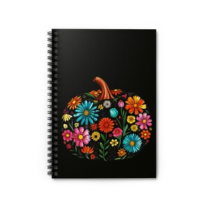 Può includere: Un quaderno a spirale con copertina nera con un colorato design di zucca floreale. La zucca è piena di vari fiori nei toni del blu, arancione, rosa e giallo, con un gambo marrone.