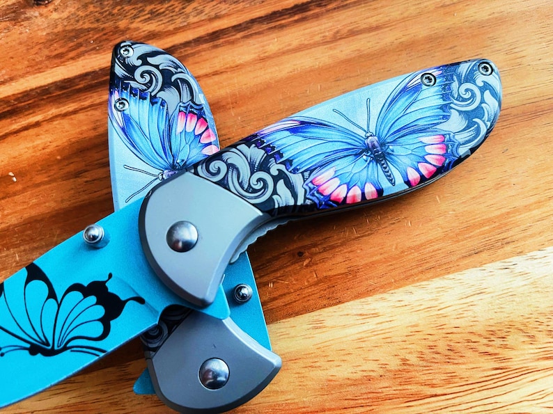 May include: A blue and silver pocket knife with a butterfly design. The knife has a black handle and a silver blade. The butterfly design is on both sides of the knife.