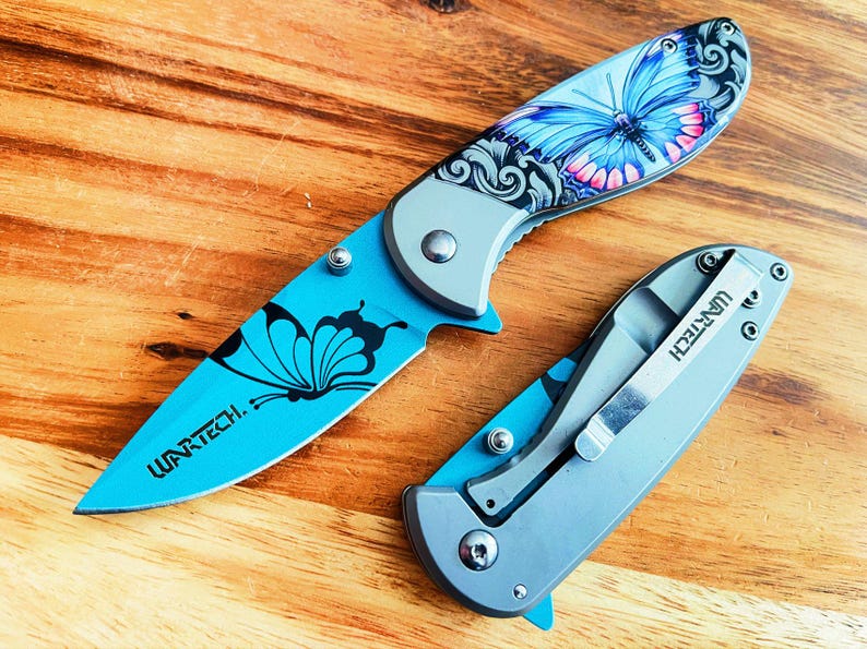 May include: Two blue pocket knives with butterfly designs. The knives have silver blades and handles. The larger knife has the text "WARTECH." on the handle. The smaller knife has the text "WARTECH." on the side of the handle.