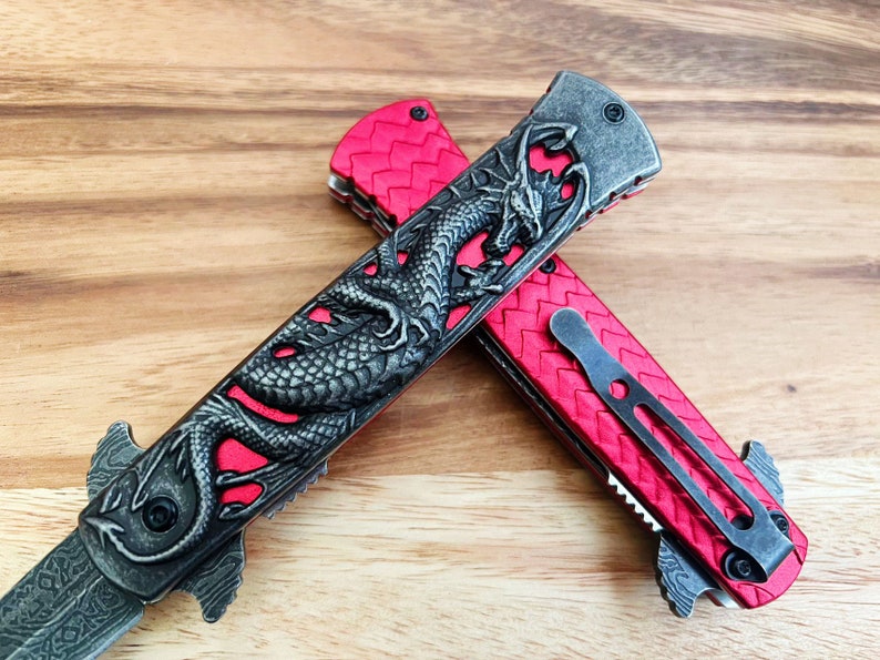May include: Two red pocket knives with a dragon design on the handle. The knives are open and the blades are visible.