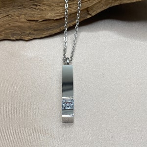 Puede incluir: Un collar de cadena de plata con un colgante de plata que presenta una sola piedra de circonita cúbica transparente.