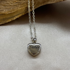 May include: Silver heart-shaped pendant necklace with the word "Sister" engraved on it.