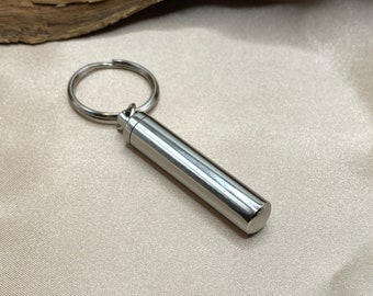 May include: A silver keychain with a small, cylindrical container attached to a silver ring.