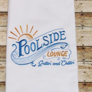 May include: White kitchen towel with blue and orange embroidery that reads "Poolside Lounge Grillin' and Chillin'".