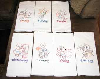 May include: Set of seven white kitchen towels, each embroidered with a different cartoon animal and the day of the week. Designs include a sleeping cat, a bird, a mouse, a duck, a bunny, a dog, and a squirrel.