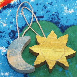 May include: A wooden sun and moon ornament with a blue and yellow paint finish. The sun and moon are connected by a twine string.