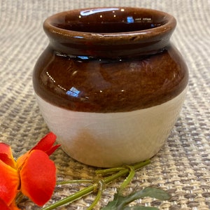 May include: A small, brown and white ceramic jar with a rounded shape. The jar has a brown glaze on the top half and a white glaze on the bottom half.