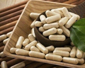May include: A wooden spoon and a wooden tray hold numerous beige capsules. The capsules are cylindrical and appear to be filled with a powder. A green leaf is visible on the right side of the image. The capsules are likely a dietary supplement.