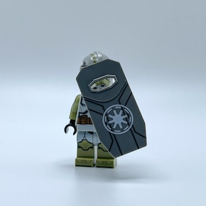 May include: A gray and white Lego minifigure of a clone trooper holding a gray shield with a white symbol of the Galactic Republic.