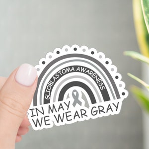 May include: A gray and white sticker with a rainbow design and the text "In May We Wear Gray" and "Glioblastoma Awareness".