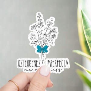 May include: A white sticker with a black line drawing of a bouquet of flowers tied with a blue ribbon. The text "Osteogenesis Imperfecta Awareness" is below the flowers.