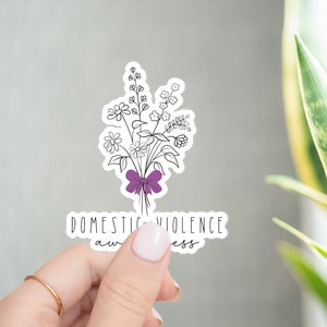 May include: A white sticker with a black line drawing of a bouquet of flowers tied with a purple ribbon. The text "Domestic Violence Awareness" is written below the flowers.