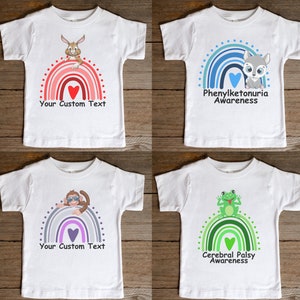 May include: Four white t-shirts with rainbow designs and animal illustrations. The shirts feature the text "Your Custom Text", "Phenylketonuria Awareness", "Cerebral Palsy Awareness", and a heart.