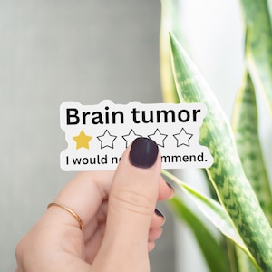 May include: A white rectangular sticker with black text that reads Brain tumor and I would not recommend. The design features a five-star rating system with one yellow star filled in and four empty outlined stars, mimicking a negative online review.