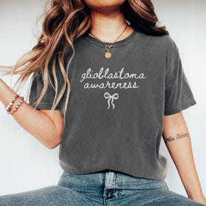 May include: A gray t-shirt with the text "glioblastoma awareness" and a white ribbon printed on the front.