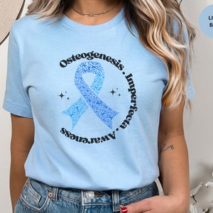 May include: Light blue t-shirt with a blue ribbon made of smaller ribbons. The ribbon is in a circle with the text "Osteogenesis Imperfecta Awareness" around it.