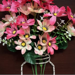 May include: A bouquet of pink and white flowers with green stems arranged in a wire jar. The flowers are in a wooden frame.