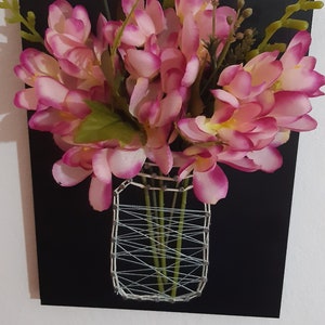 May include: A pink flower arrangement in a string art vase on a black background.
