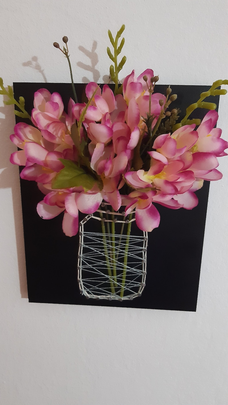 May include: A pink flower arrangement in a string art vase on a black background.