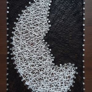 May include: A rectangular string art piece featuring a crescent moon design. The moon is crafted with white string against a black background. The artwork is framed with small silver nails on a wooden surface.