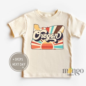 May include: A cream colored t-shirt with a retro graphic of the state of Oregon with a sunburst design and the word "Oregon" in a vintage font.