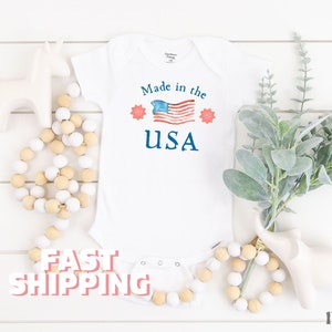 May include: White baby onesie with a red, white, and blue American flag and the text "Made in the USA".