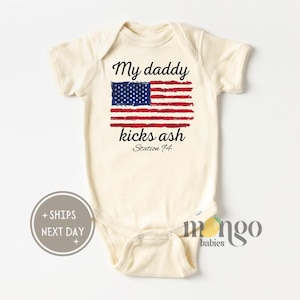 Peut inclure: Un body bébé blanc avec un drapeau américain rouge, blanc et bleu et le texte "My daddy kicks ash Station 74".
