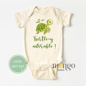 May include: A cream-colored baby onesie with a green cartoon turtle and the text "Turtle-y adorable!" printed on the front.