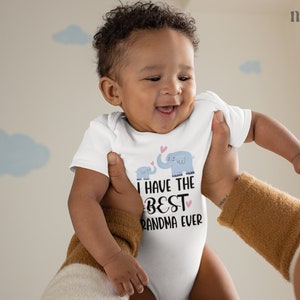 May include: A white baby onesie with a blue and gray elephant graphic and the text "I have the best grandma ever".