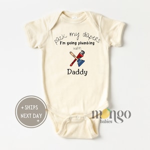 May include: A cream-colored baby onesie with the text "pack my diapers I'm going plumbing with Daddy" and a cartoon image of a wrench and plunger.