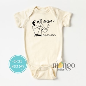 Może przedstawiać: Kremowy śpioszek dla niemowlęcia z czarno-białym rysunkiem Freddiego Mercury'ego śpiewającego z tekstem "MAMA! OO-OO-OOOH!" nadrukowanym z przodu.