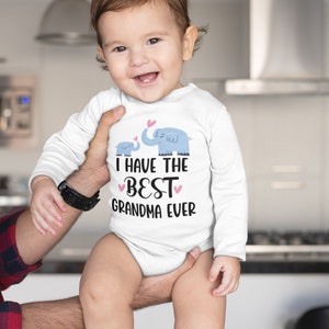 May include: A white long-sleeve baby onesie with a graphic of two blue elephants and the text "I have the best grandma ever" in black with pink hearts.