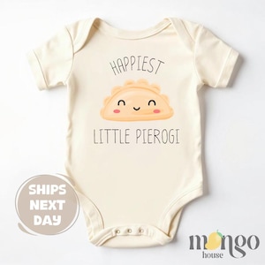 May include: Cream-colored baby bodysuit with the text "Happiest Little Pierogi" and a smiling pierogi graphic. The bodysuit has short sleeves and snap closures. The design is printed in black and orange.