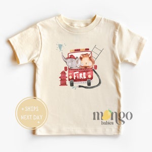 May include: A cream colored short-sleeved t-shirt with a red fire truck with an elephant and a lion riding in it. The fire truck has the word "FIRE" on the side. There is a fire hydrant in front of the truck. The shirt has the words "mango babies" on the bottom.