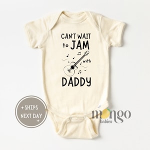 May include: A cream-colored baby onesie with black text that reads "Can't wait to JAM with DADDY" and a black and white illustration of a guitar with musical notes.