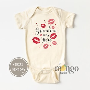 May include: A cream-colored baby onesie with a red and pink lip print and the text "Grandma was Here".