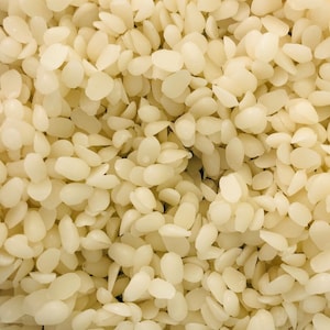 May include: A close-up shot of numerous off-white, oval wax beads. The beads are densely arranged, forming a textured pattern. The lighting accentuates the smooth, slightly transparent nature of the wax. This image is suitable for products related to candle making or cosmetic supplies.