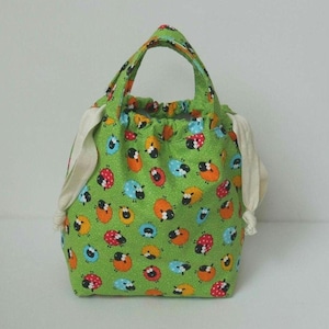 May include: A green fabric drawstring bag with a white handle. The bag is decorated with a pattern of black sheep and red ladybirds on a green background.
