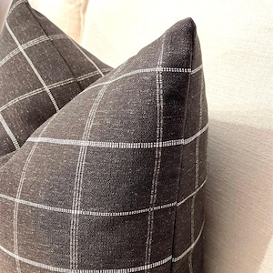 K&ouml;nnte beinhalten: Zwei schwarze und wei&szlig;e karierten Kissen mit einer dezenten Textur. Die Kissen liegen auf einem wei&szlig;en Sofa.