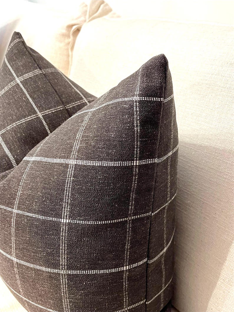 K&ouml;nnte beinhalten: Zwei schwarze und wei&szlig;e karierten Kissen mit einer dezenten Textur. Die Kissen liegen auf einem wei&szlig;en Sofa.