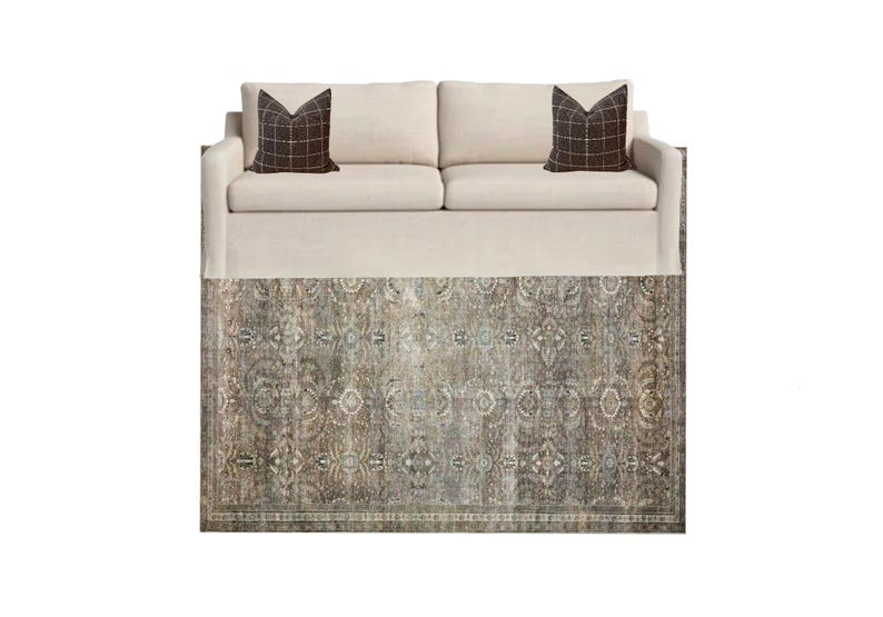 K&ouml;nnte beinhalten: Ein wei&szlig;es Sofa mit zwei braunen, gemusterten Kissen steht auf einem gemusterten Teppich in Braun-, Beige- und Blaut&ouml;nen.