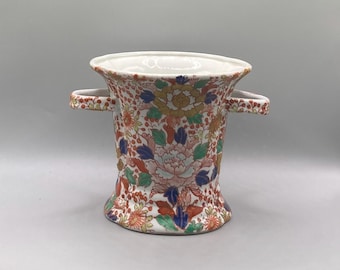 May include: A white porcelain vase with two handles. The vase is decorated with a floral pattern in shades of red, blue, green, and yellow.
