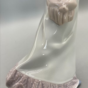 Puede incluir: Una figurita de porcelana de una mujer con un vestido azul y blanco con un bolso rosa. El vestido tiene un ribete floral rosa.