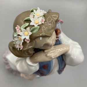 Puede incluir: Una figurita de porcelana de una ni&ntilde;a con cabello casta&ntilde;o que lleva un vestido blanco y una corona de flores. Ella se est&aacute; sosteniendo la cabeza con las manos y tiene una expresi&oacute;n melanc&oacute;lica en su rostro.