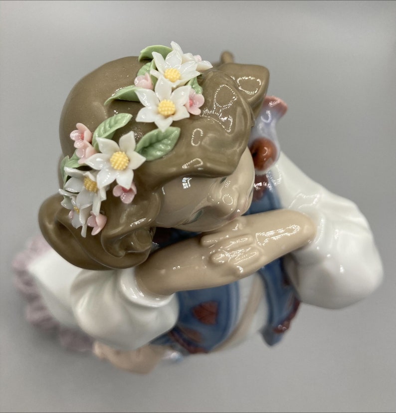Puede incluir: Una figurita de porcelana de una ni&ntilde;a con cabello casta&ntilde;o que lleva un vestido blanco y una corona de flores. Ella se est&aacute; sosteniendo la cabeza con las manos y tiene una expresi&oacute;n melanc&oacute;lica en su rostro.