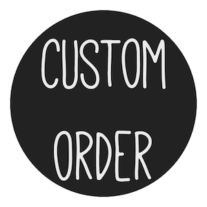 May include: A black circle with the words "CUSTOM ORDER" in white, handwritten-style lettering. The text is centered within the circle, creating a simple, bold design.