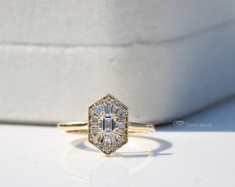 May include: A gold ring featuring a hexagonal cluster setting with a central emerald-cut diamond surrounded by radiating baguette-cut diamonds. The band is thin and polished gold. The text Elista Jewel is visible in the lower right corner.