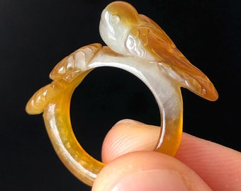 Puede incluir: Un anillo de jade tallado con un diseño de pájaro. El anillo es de color amarillo claro con un centro blanco.